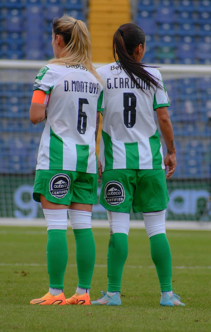 Back view of two women soccer players in matching uniforms on the field during a match.